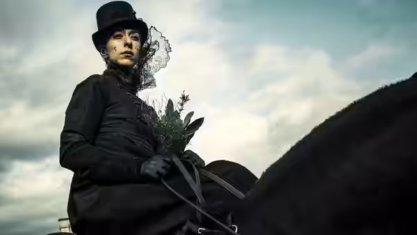 Woman in black hat and veil riding a horse holding flowers
