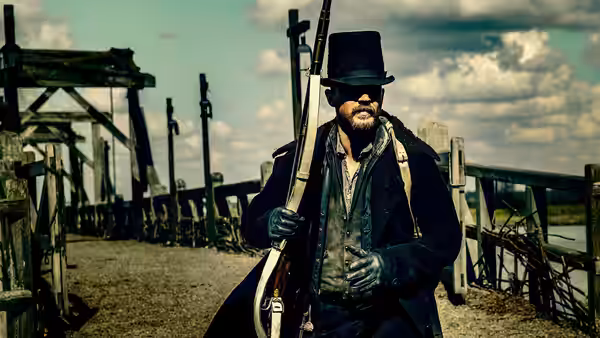 James Keziah Delaney (Tom Hardy) holding a rifle on a wooden bridge
