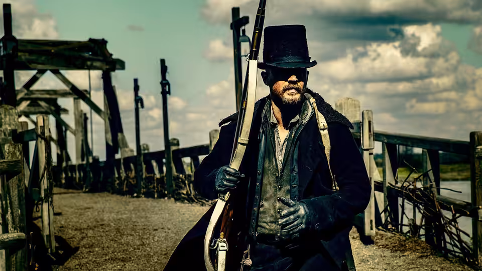 James Keziah Delaney (Tom Hardy) holding a rifle on a wooden bridge