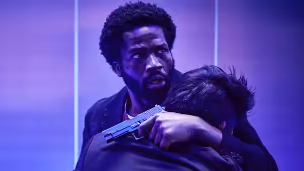 Elliot Finch (Sope Dirisu) grips a handgun while holding another man