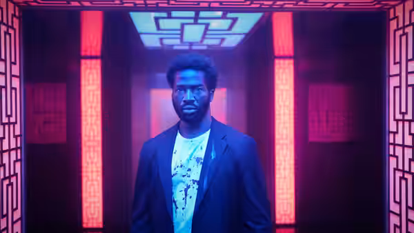 Elliot Finch (Sope Dirisu) stands inside a red-lit patterned elevator