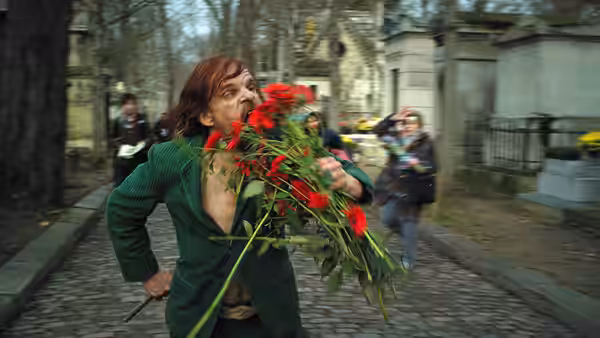 man in green jacket holds large bouquet of red roses in cemetery