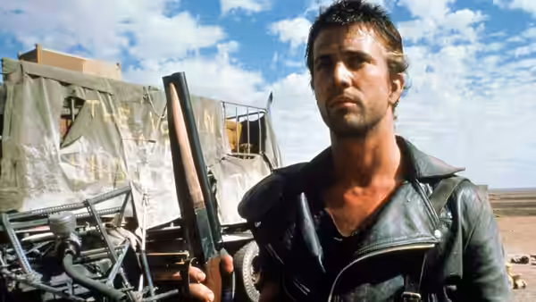 Max Rockatansky (Mel Gibson) holding a shotgun beside a wrecked vehicle in the desert