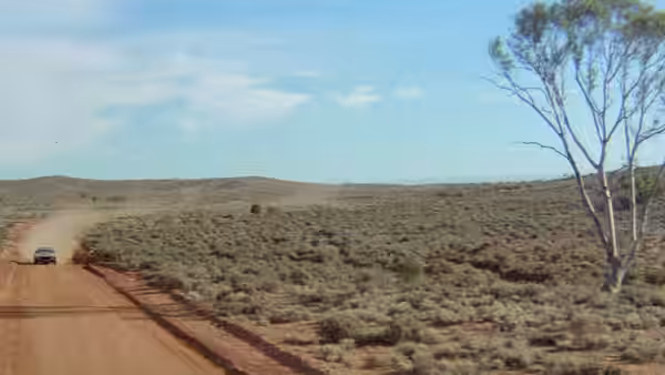 A car driving on a dirt road through arid scrubland leaving a dust trail