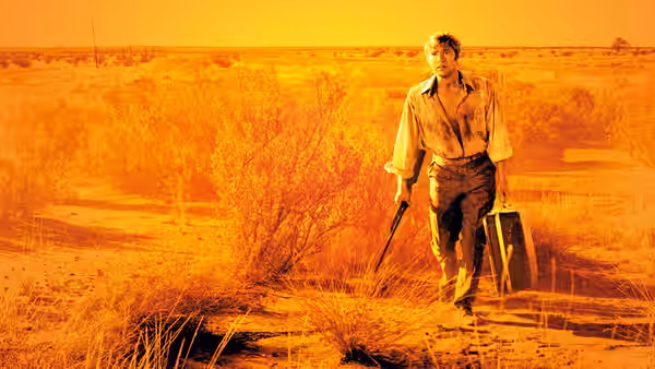 John Grant (Gary Bond) walks through the desert carrying a rifle and suitcase