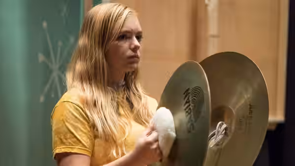 Kayla (Elsie Fisher) holding cymbals in a school music room