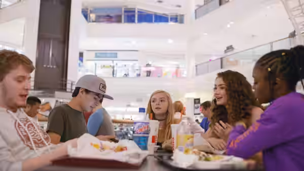 Kayla (Elsie Fisher) sitting with friends at a mall food court