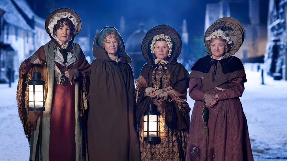 Four women in bonnets and cloaks holding lanterns on a snowy street at night