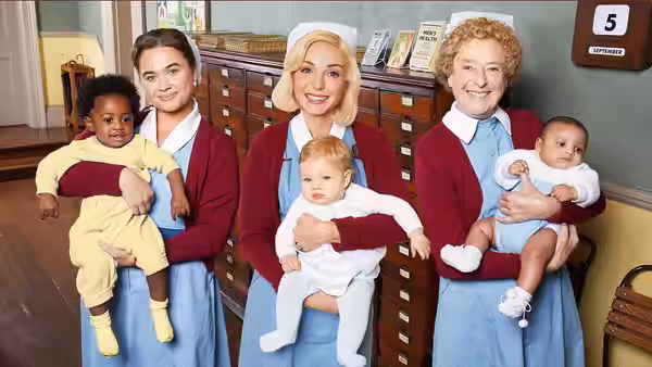 Three nurses holding babies in front of a medical records cabinet