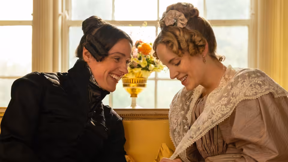 Anne Lister (Suranne Jones) and Ann Walker (Sophie Rundle) smiling closely indoors by a window