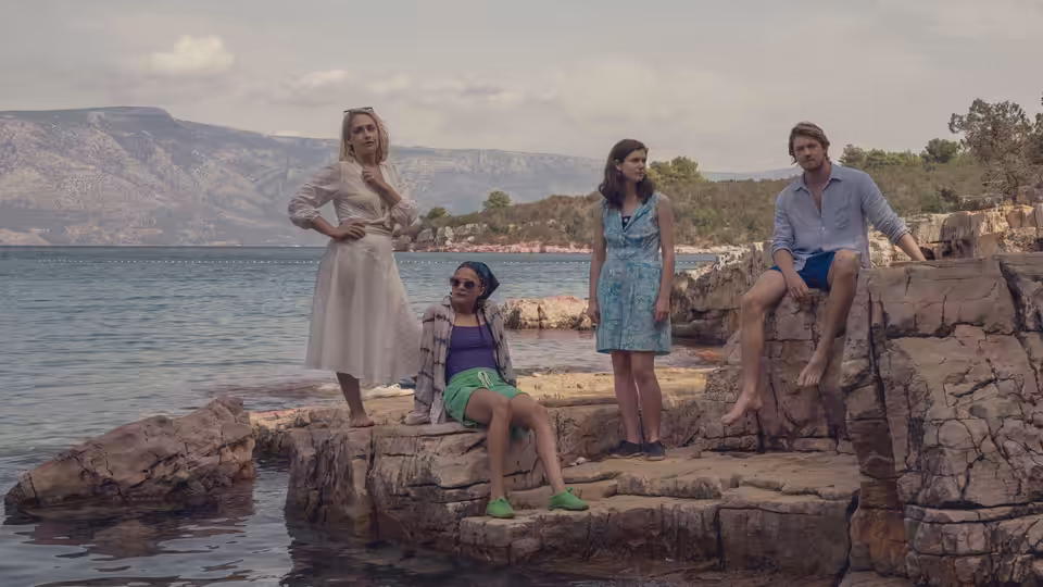 Four friends gathered on seaside rocks with mountains in the background