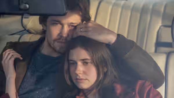 Young man resting his hand on a woman's head inside a car