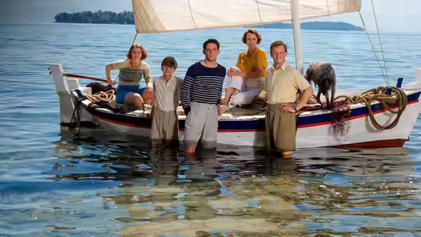 Group stands in the sea beside a small sailboat