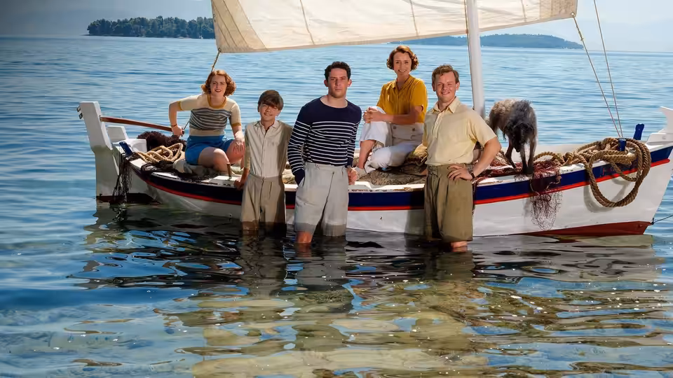 Group stands in the sea beside a small sailboat