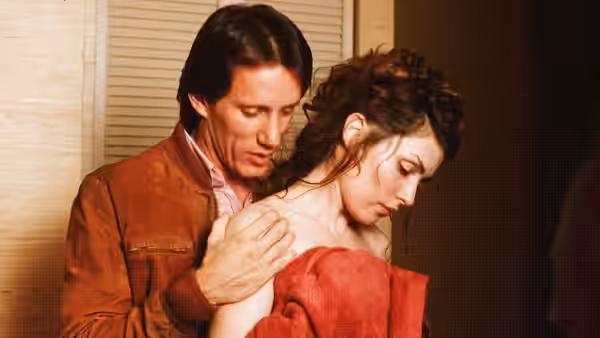 a man in a brown jacket standing behind a woman wrapped in a red towel