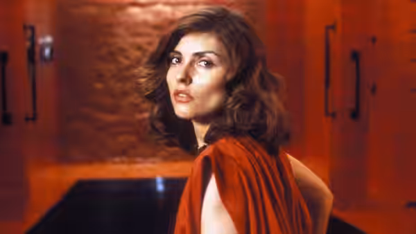 a woman with wavy brown hair wearing a red garment in a hallway
