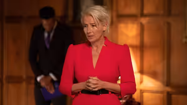 Vivienne Rook (Emma Thompson) stands with clasped hands in a formal room