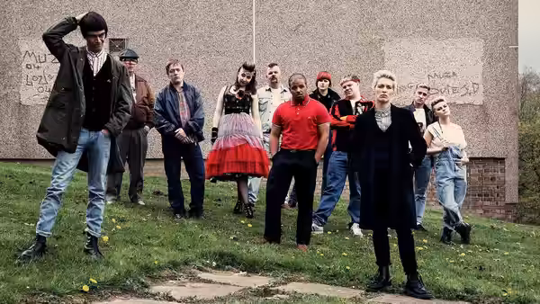 Young adults in 1980s clothes standing together on grass before a wall