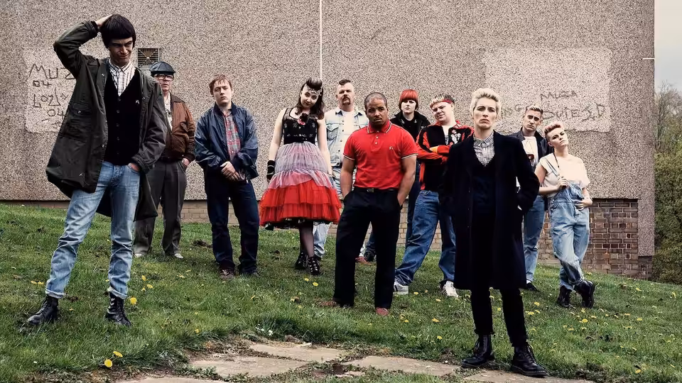 Young adults in 1980s clothes standing together on grass before a wall