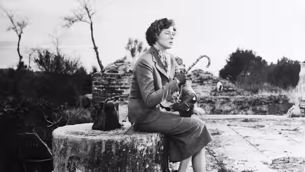 Ingrid Bergman as Katherine Joyce sitting on stone in ruins holding an umbrella