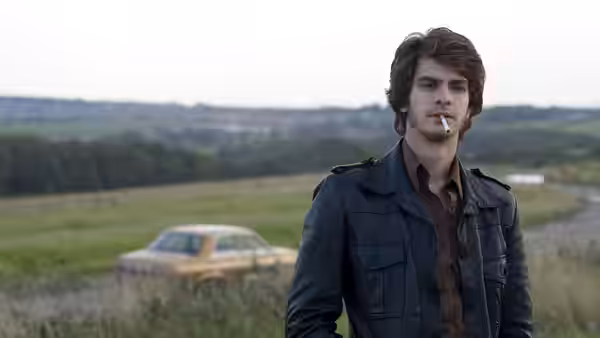 Eddie Dunford (Andrew Garfield) standing in a field with a cigarette in his mouth