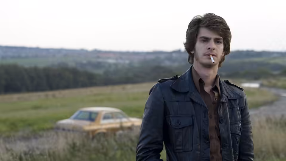 Eddie Dunford (Andrew Garfield) standing in a field with a cigarette in his mouth