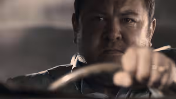 A man gripping a steering wheel with a stern expression on his face