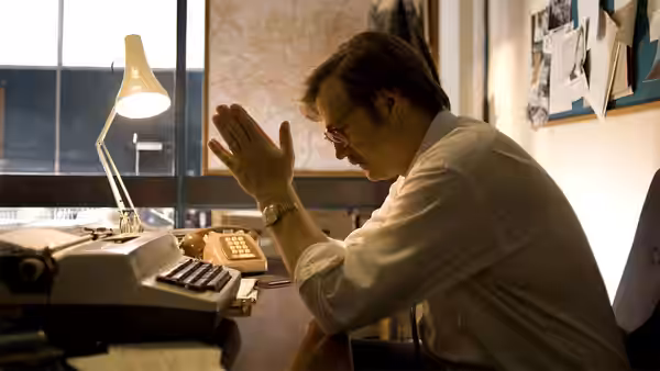 A man in a white shirt leaning over a typewriter in an office