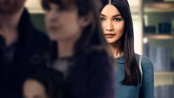 Gemma Chan as Anita looking forward in a blurred indoor space