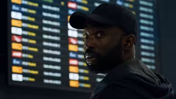 Paapa Essiedu as George looks back in front of airport departure boards