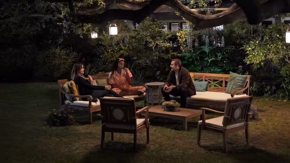 Three people seated around a table talking in a garden at night