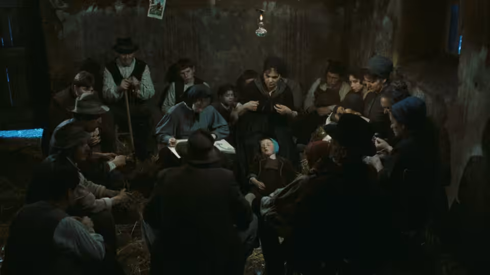 Farmers gather around a woman lying in bed inside a dim farmhouse room