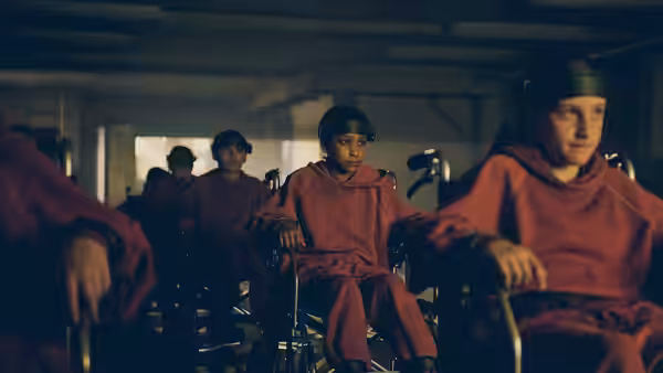 Melanie sits among children in orange uniforms inside a dim room