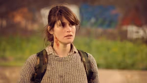Helen Justineau stands outdoors with a backpack and blood on her neck
