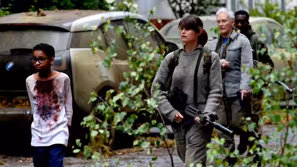 Melanie walks through overgrown streets as Helen carries a rifle nearby