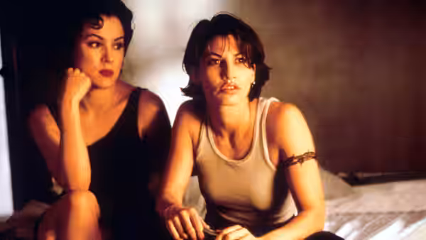 Violet (Jennifer Tilly) and Corky (Gina Gershon) sitting side by side on a bed