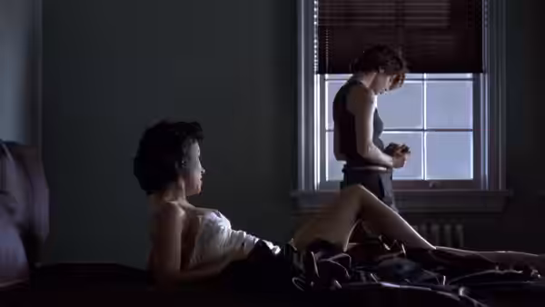Violet (Jennifer Tilly) reclining on a bed as Corky (Gina Gershon) stands nearby