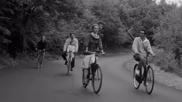 Catherine and three men ride bicycles along a country road