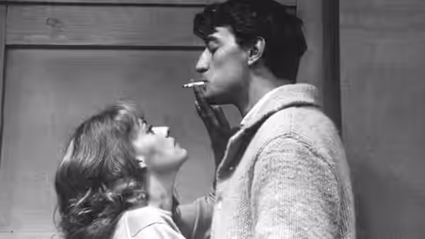 A young man stands close to a woman indoors