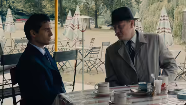 Napoleon Solo (Henry Cavill) talks with a fedora-wearing man at an outdoor café