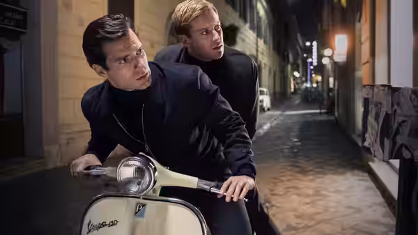 Napoleon Solo (Henry Cavill) and Illya Kuryakin (Armie Hammer) peer behind them on a Vespa