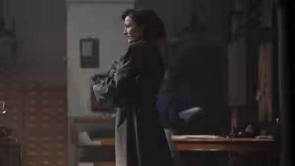 Jean Leslie (Kelly Macdonald) stands with folded arms in a dim office