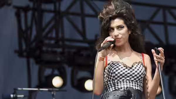 Amy Winehouse singing into a microphone on an outdoor stage