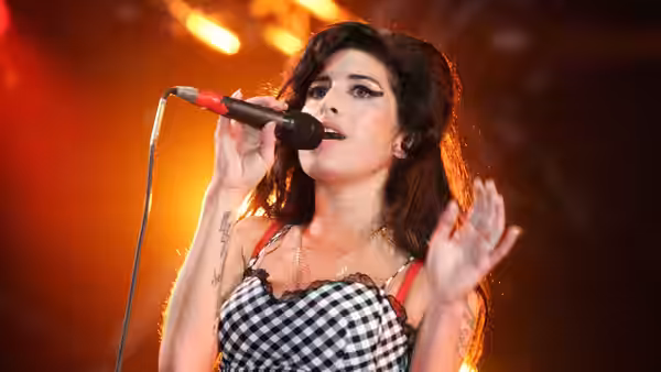 Amy Winehouse performing with a microphone on a brightly lit stage