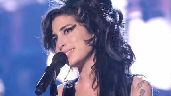 Amy Winehouse smiling while singing into a microphone on stage