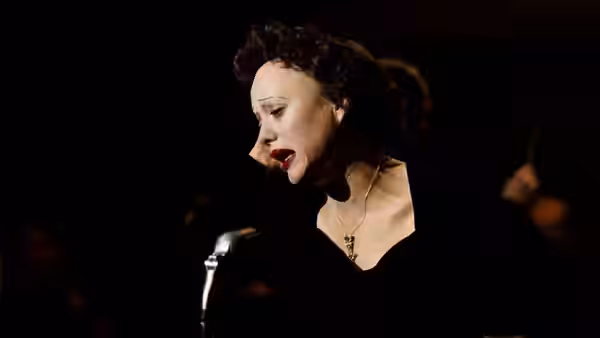Edith Piaf (Marion Cotillard) sings into a microphone on a dark stage