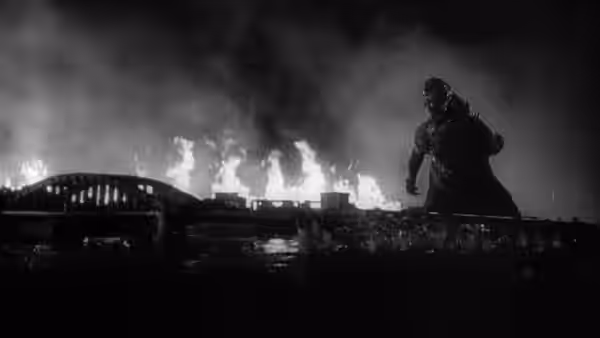 Godzilla silhouetted against a burning city with a bridge in flames