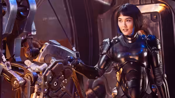 Mako Mori (Rinko Kikuchi) reaches toward complex machinery while wearing dark metallic armor