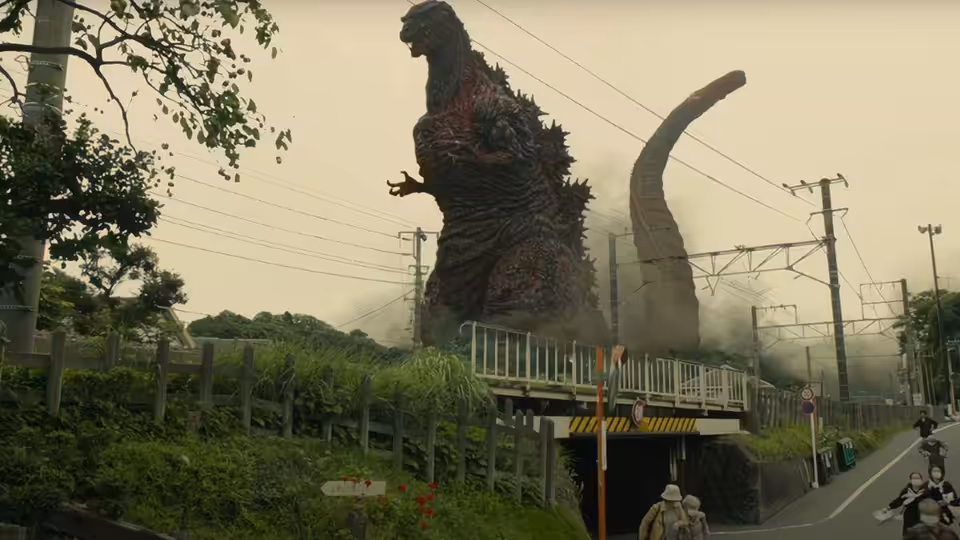 Godzilla rises beside a railway overpass as pedestrians flee along the road