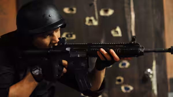 helmeted soldier aims rifle through holes in a damaged door
